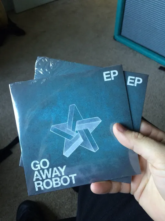 A hand holding two CD copies of the Go Away Robot EP
