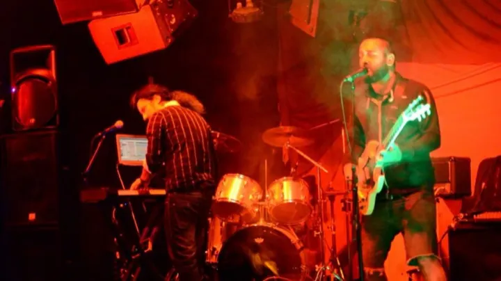 The band playing live with keys, drums and guitar under orange stage light
